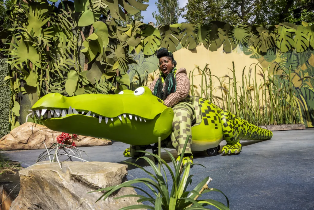 Person riding a large crocodile prop.